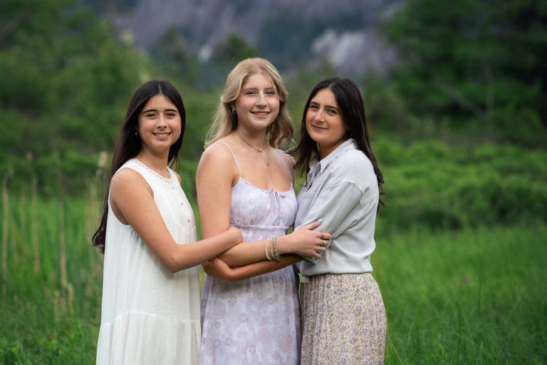 Family Portrait of three sisters linked through arms standing in grass field