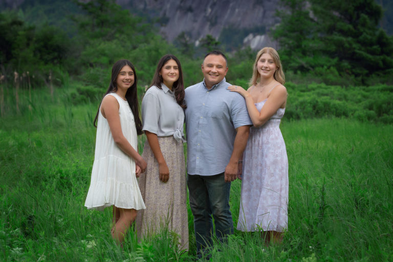 Family Portrait of dad with three daughters standing in green grass field