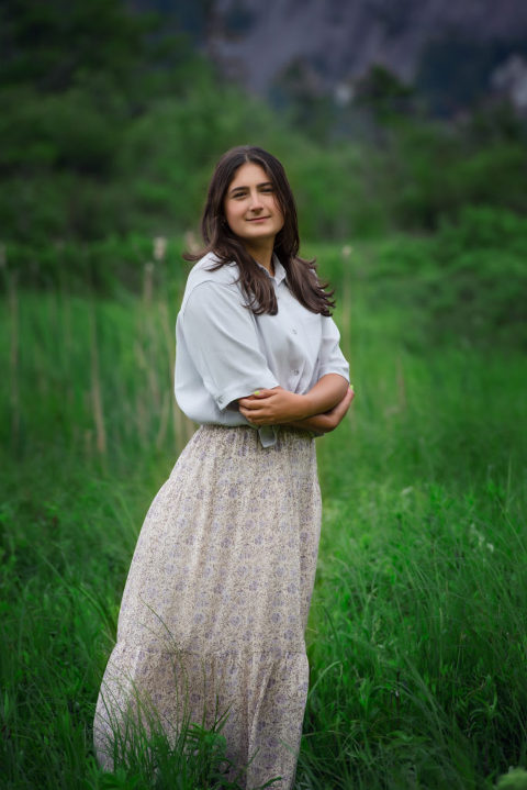 Family Portrait girl wearing floral skirt and light blue shirt, arms folded at waist standing in green grass